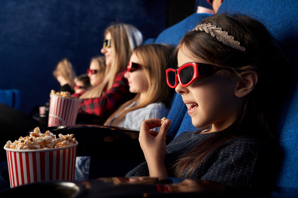 Família no cinema vendo filme e comendo pipoca — Foto: Freepik