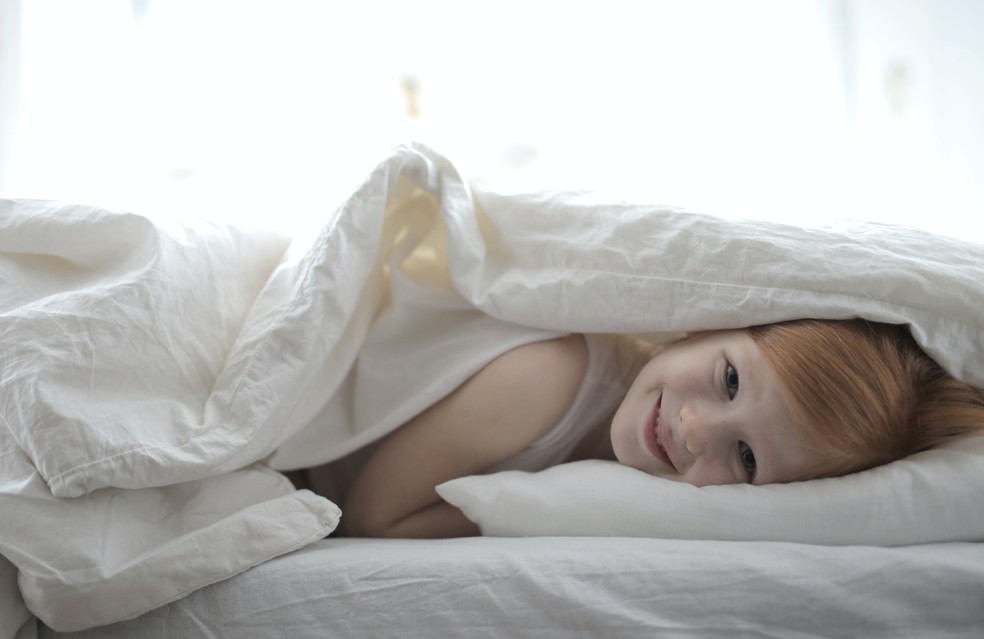 Criança com frio embaixo das cobertas — Foto: Pexels/Andrea Piacquadio