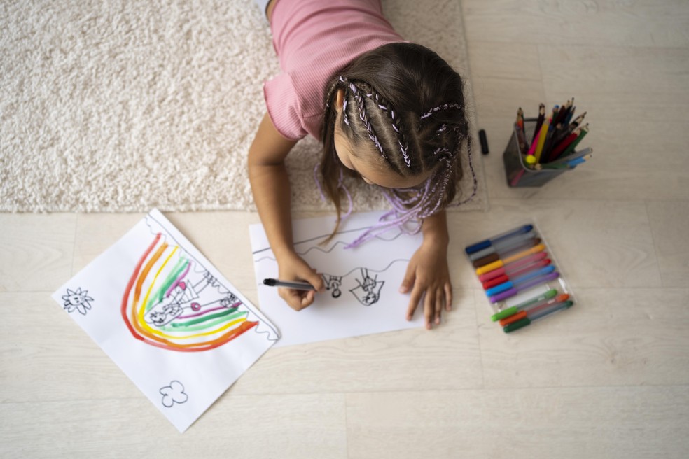 Menina sentada no chão fazendo desenhos com canetinhas — Foto: Freepik