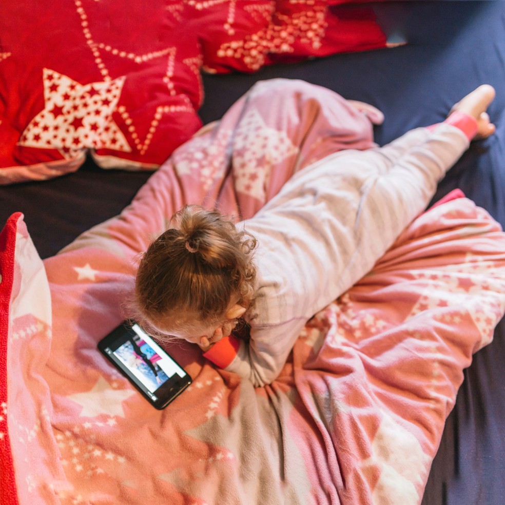 Menina deitada na cama mexendo no celular — Foto: Freepik
