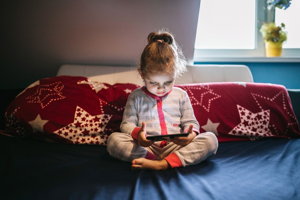 Menina sentada na cama mexendo no celular — Foto: Freepik