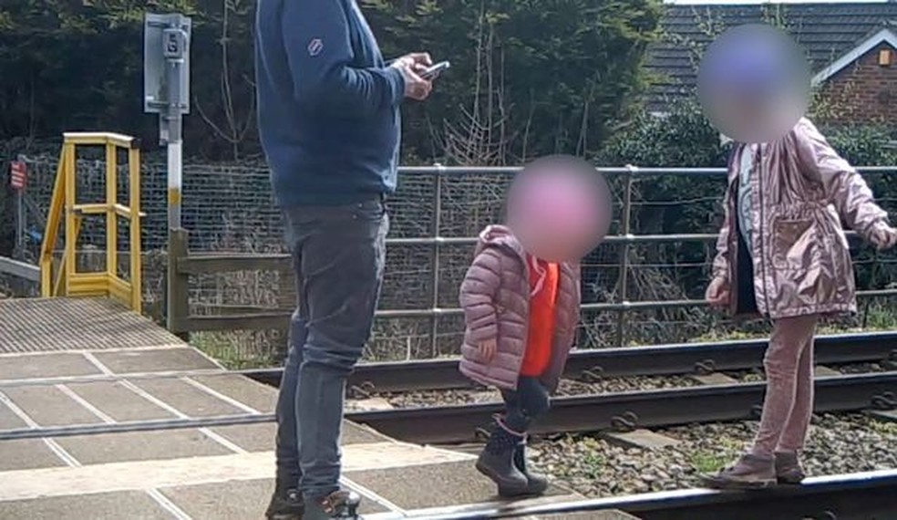 Pai ao celular, enquanto crianças brincam nos trilhos do trem — Foto: Reprodução/ Youtube